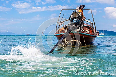 Krabi, Thailand - February 12, 2019: The driver of a longtail motorboat drives a motor with a long drive and a propeller. Sailor Editorial Stock Photo