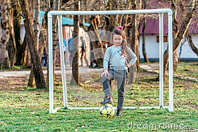 Young Caucasian goalkeeper girl with flushed face posing by outdoor football goal with foot put on ball looking into camera Editorial Stock Photo