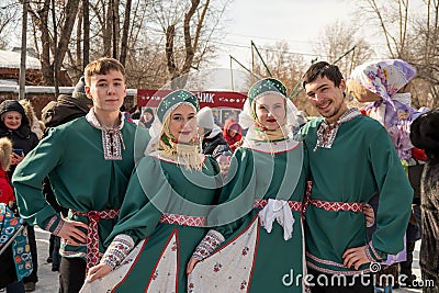 Young people in Russian ethnic costumes pose against the backdrop of a crowd of people at the Farewell to Winter holiday in a city Editorial Stock Photo