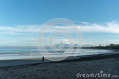 KUTA.BALI-MARCH 13 2019: People on the beach of tropical sea. with traditional boat, wave, mountain and clouds on the background Editorial Stock Photo