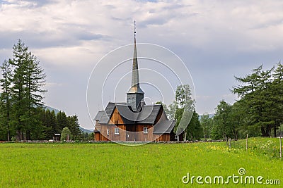 A vibrant green field and the historic Kvikne kirke, an old wooden church surrounded by lush green trees Stock Photo