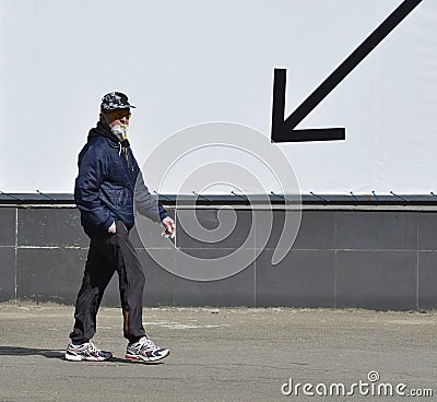 A man wearing a mask and goggles walks past a black arrow pointing downwards Editorial Stock Photo