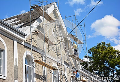 Contractors plastering house facade outdoor. Painting and plastering exterior house scaffolding wall with asbestos roof repair Stock Photo