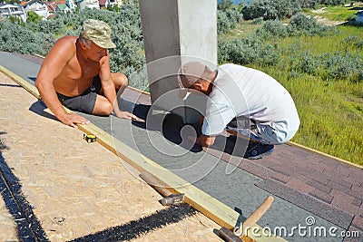 Roofers installing Asphalt Shingles on house roofing construction. Roofing Contractors laying Asphalt Shingles roof tiles Editorial Stock Photo