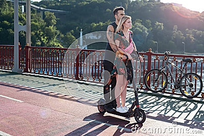 Kyiv, Ukraine - July 11, 2020. Pedestrian bridge. Attractive couple in love riding one electric push scooter together Editorial Stock Photo