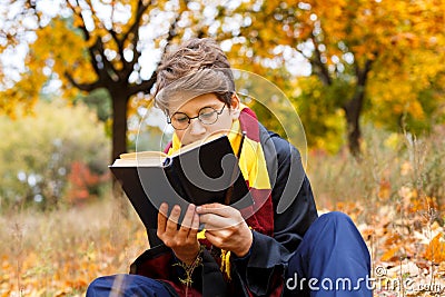 Cute pretty boy in costume of Harry Potter and scarf plays as a magician, reads book in autumn Editorial Stock Photo