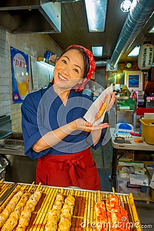 KYOTO, JAPAN - JULY 05, 2017: Unidentified smiling woman holding in her hand a brochette, sold at Nishiki Market in Editorial Stock Photo