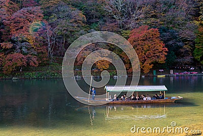 Unidentified tourists on wooden boat enjoy autumn colors along Hozu-gawa river at Arashiyama Editorial Stock Photo