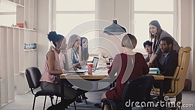 L'entraîneur féminin heureux d'affaires donne des guides des employés Travail d'équipe multi-ethnique par la table lors de la réu L'entraîneur féminin heureux d'affaires donne des guides des employés Travail d'équipe multi-ethnique par la table lors de la réu