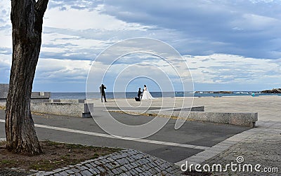 Wedding photographer working on a beach promenade. Sunset, cloudy grey sky. La Coruna, Spain. Editorial Stock Photo