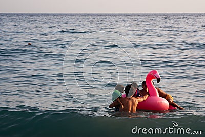 Inflatable latex pink flamingo floating in the sea. Father and children Editorial Stock Photo