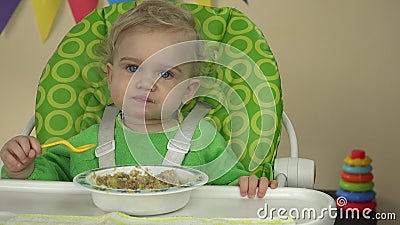 La pratica della bambina mangia il gruel con il cucchiaio si siede sulla sedia del bambino 4K stock footage La pratica della bambina mangia il gruel con il cucchiaio si siede sulla sedia del bambino 4K stock footage