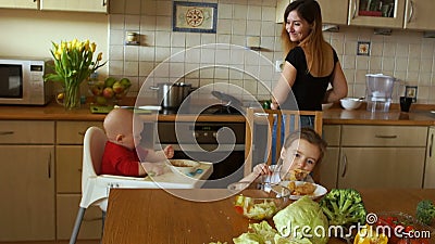 La ragazza prepara la cena nella cucina allo stesso tempo che cerca due bambini - un ragazzo e una ragazza Casalinga sul lavoro archivi video La ragazza prepara la cena nella cucina allo stesso tempo che cerca due bambini - un ragazzo e una ragazza Casalinga sul lavoro archivi video