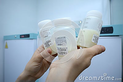 Lab assistant hand holding breast milk storage containers with human milk, freezers on a background. Human Milk Bank laboratory Stock Photo