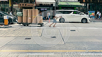 Labor or worker pulling heavily loaded trolley or barrow on traffic street Editorial Stock Photo