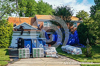 Laborers replacing a roof on a house with a blue dumpster and supplies in the driveway Editorial Stock Photo