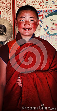 young tibetan buddhist nun in front of a highly decorated wall of her monastery Editorial Stock Photo
