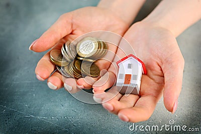 Lack of money to buy a house concept. Woman holds toy house in one hand and handful of coins in another. Stock Photo