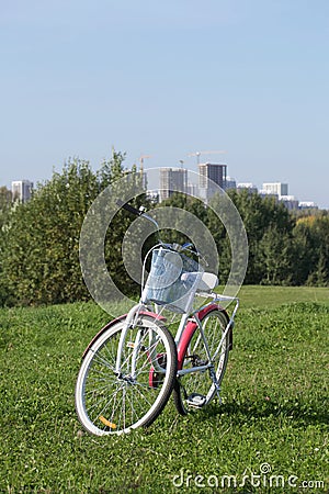 Ladies` bike in red and white. Stands in the park on the lawn. Multi-storey buildings under construction are visible on the Stock Photo