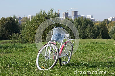 Ladies` bike in red and white. Stands in the park on the lawn. Multi-storey buildings under construction are visible on the Stock Photo