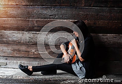 The lady in black suit is sitting on grunge surface ground floor,hold violin with bow in arms ,turn face down to violin,vintage an Stock Photo