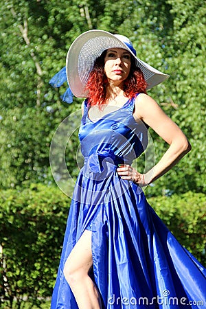 a lady in a blue dress and a white hat on a green lawn. a woman in a hat and a long dress with a train on the skirt in the Park, Stock Photo