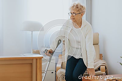 Lady with a cane gets up from a chair from a room in a retirement home Stock Photo