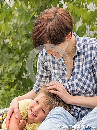 Lady with child playing outdoor. Beautiful boy put head on mother`s knees. Stock Photo