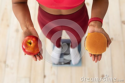 Lady Choosing Between Burger And Apple Standing On Weight-Scales Indoor Stock Photo