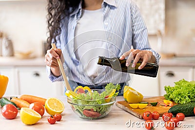 Lady cooking fresh vegetable salad, adding olive oil and seasoning to bowl, enjoying eating healthy vegetarian food Stock Photo