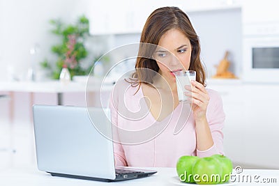 Lady drinking glass milk looking at laptop Stock Photo