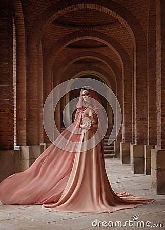 Lady in long pink dress in road coat with a hood is walking along old castle Stock Photo