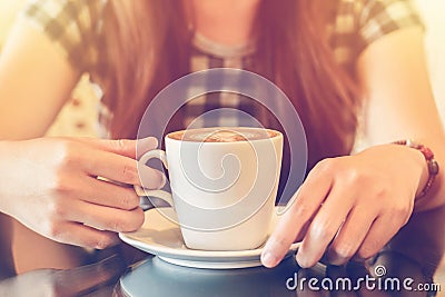 A lady picking up a cup of coffee at a coffee shop with reflections as she sits at a table Stock Photo