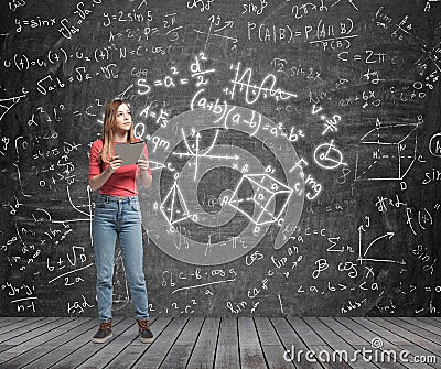 Lady is pondering about complicated math problem. Formulas and graphs are drawn on the black chalk wall. Stock Photo