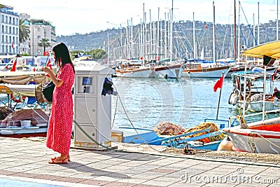 A lady in a red dress checking her phone by the Turkish Harbour Editorial Stock Photo