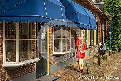 Lady with red dress and heels looking at displayed products in the antique shop in Bronkhorst Editorial Stock Photo