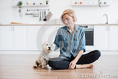 Lady sitting cross-legged in kitchen with small dog Stock Photo