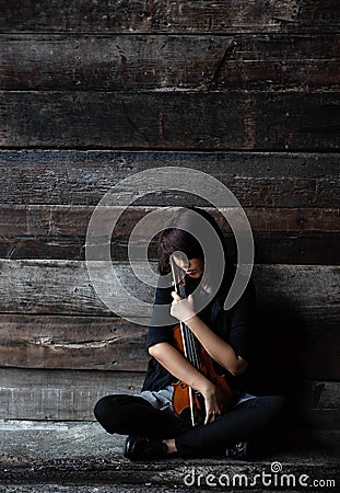 The lady is sitting on grunge surface cement floor,hold violin and bow in her arms,turn face down to violin,vintage and art style Stock Photo