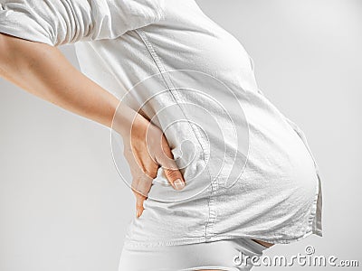 Lady in the third trimester of pregnancy. A pregnant woman in white shirt grabbed her lower back white background. The Stock Photo