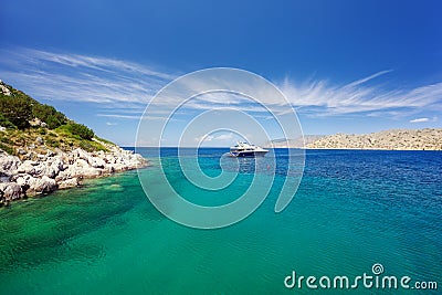 Lagoon in Hydra island, Greece. Crystal clear turquoise water. Luxury yacht with mooring ropes against the rocks Stock Photo