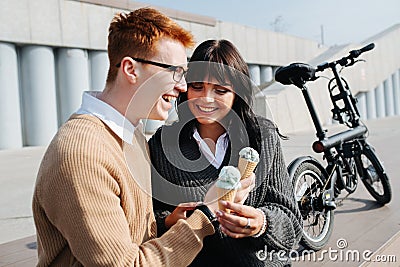 Laighing man an woman sitting outdoors, holding ice cream, talking, laughing Stock Photo
