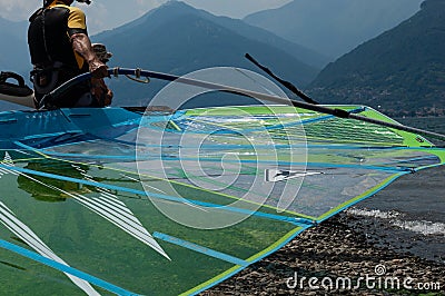 Lake Como, Italy - July 21, 2019. Man windsurfer carrying a sail into the mountain lake, surf board close-up. Alp mountains on a Editorial Stock Photo