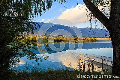 Lake in the mountains. Old wooden pier for fishing. Beautiful nature, reflection of clouds and mountains in blue water. Kyrgyzstan Stock Photo