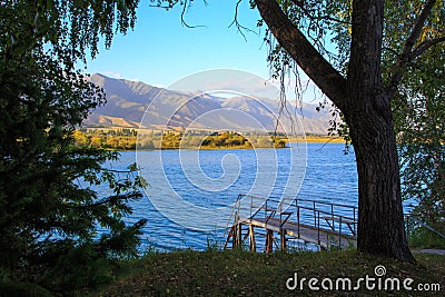 Lake in the mountains. Old wooden pier for fishing. Beautiful nature, reflection of clouds and mountains in blue water. Kyrgyzstan Stock Photo