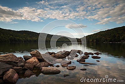 Lake with rocks in the foreground and reflection of sky and surrounding forest Stock Photo