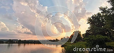 Lake shore with trees at summer sunset and gradient sky with sunbeam passing through clouds Stock Photo