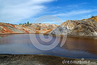 Lake surrounded by bright multi-colored clay hills against a bright blue sky. Ural Mars Stock Photo