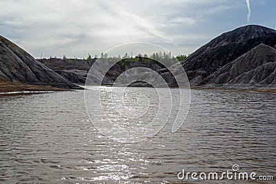 Lake surrounded by gray clay hills against the evening sky. Ural refractory clay quarries Stock Photo