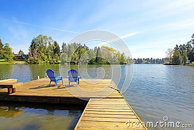 Lake waterfront with pier and two blue chairs. Stock Photo