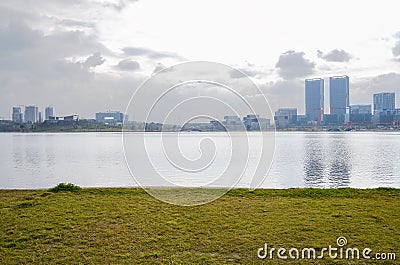 Lakeside grassy lawn with modern buildings in background on cloudy day Editorial Stock Photo
